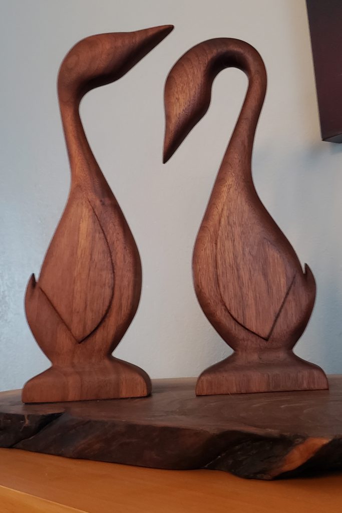 Two wooden geese facing each other standing on a live edge board